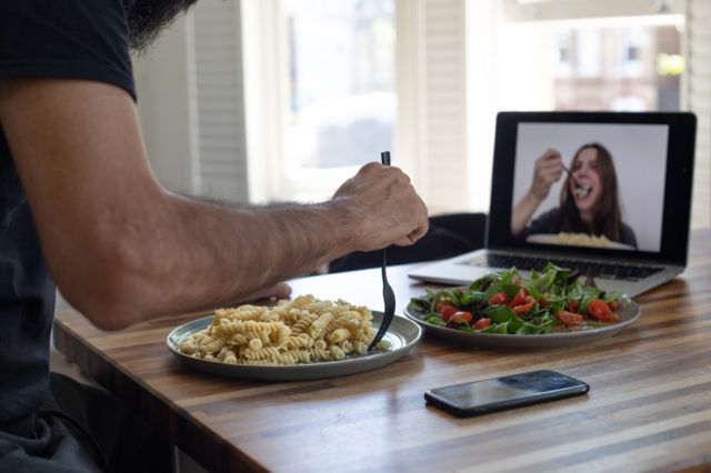 Casal comendo separado por uma tela de computador