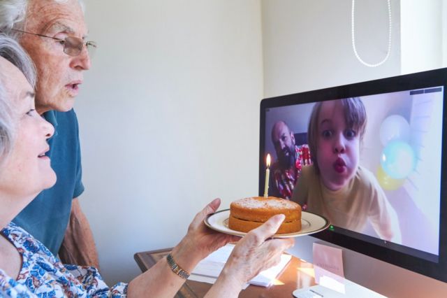 Avós com bolo de aniversário fazem videoconferência com o neto