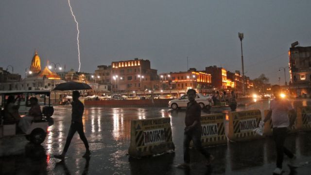 Raio cruza o céu na cidade de Jaipur, na Índia, enquanto pessoas caminham numa rua sob a chuva